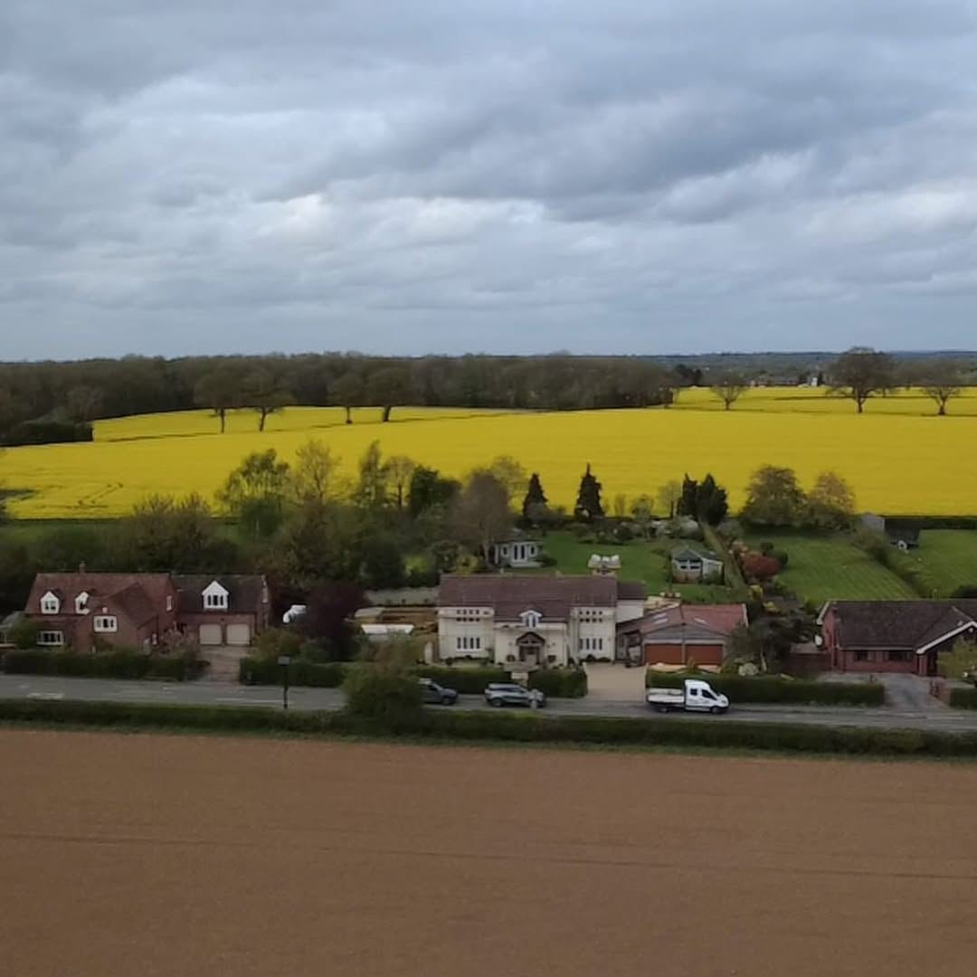 Drone view across countryside with yellow rapeseed fields behind a row of homes