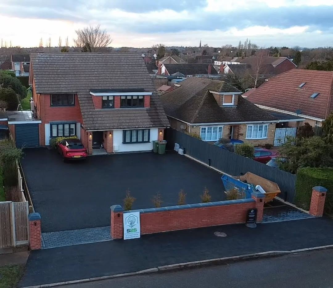 Drone view of a semi-detached house with a new dark resin driveway and brick front wall