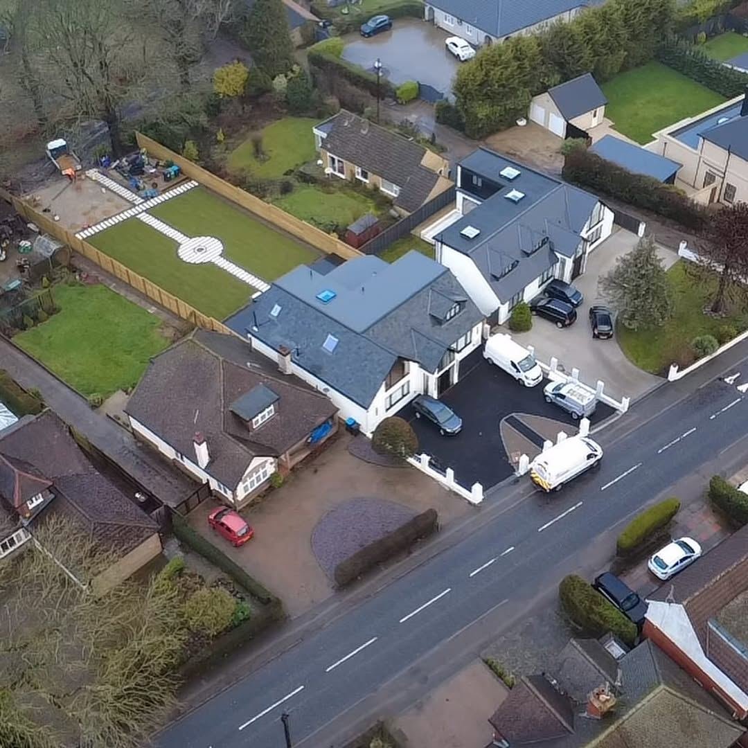 Aerial view along a road showing a finished driveway and landscaped rear garden with a circular lawn feature