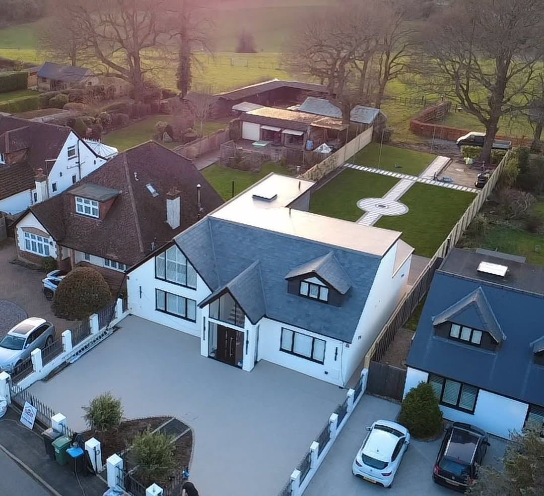Drone view of a white house with a new pale resin-bound driveway and a formal rear lawn with a circular feature
