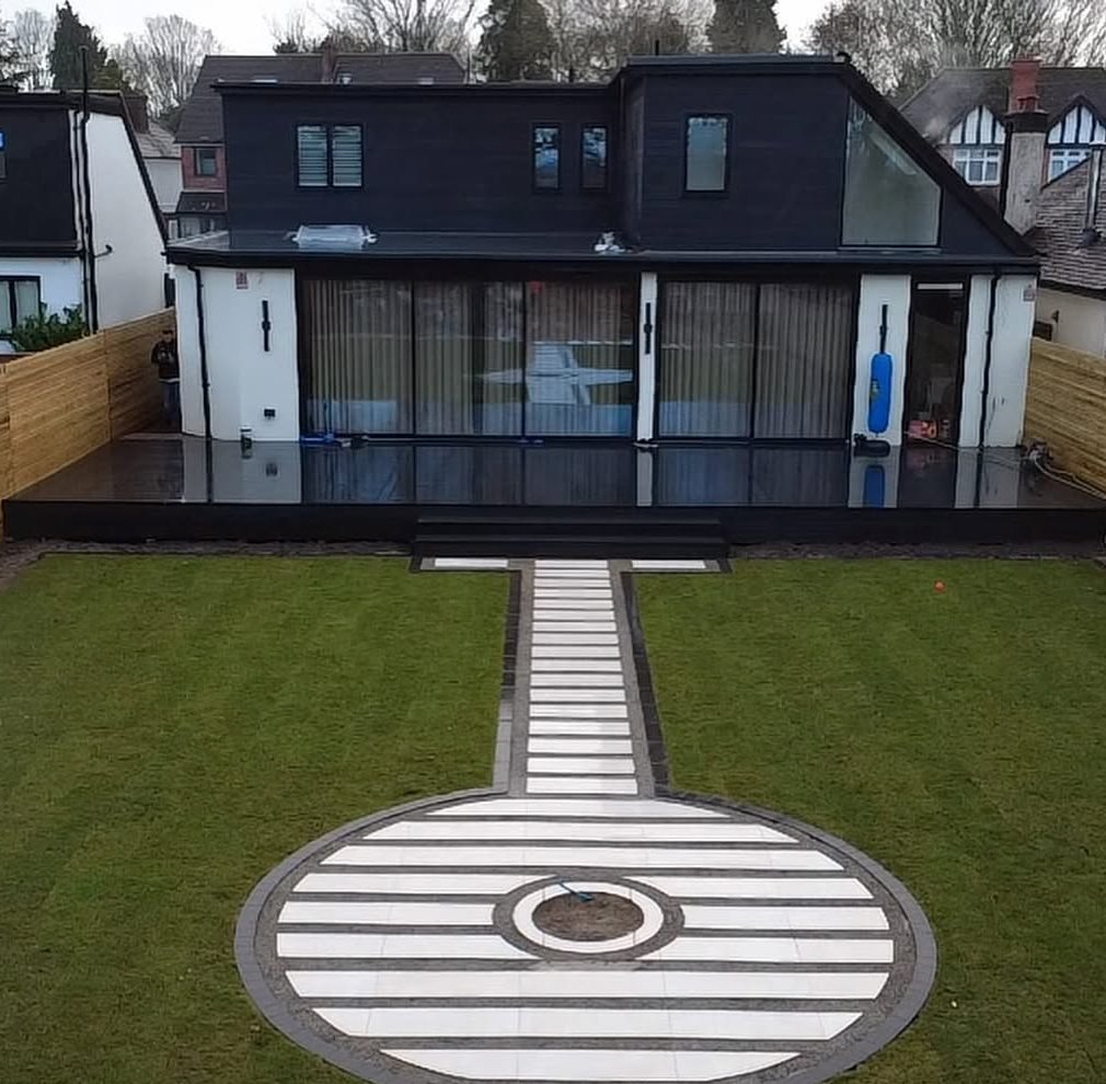 After: decking, striped lawn, paved path and circular paved feature behind a modern house