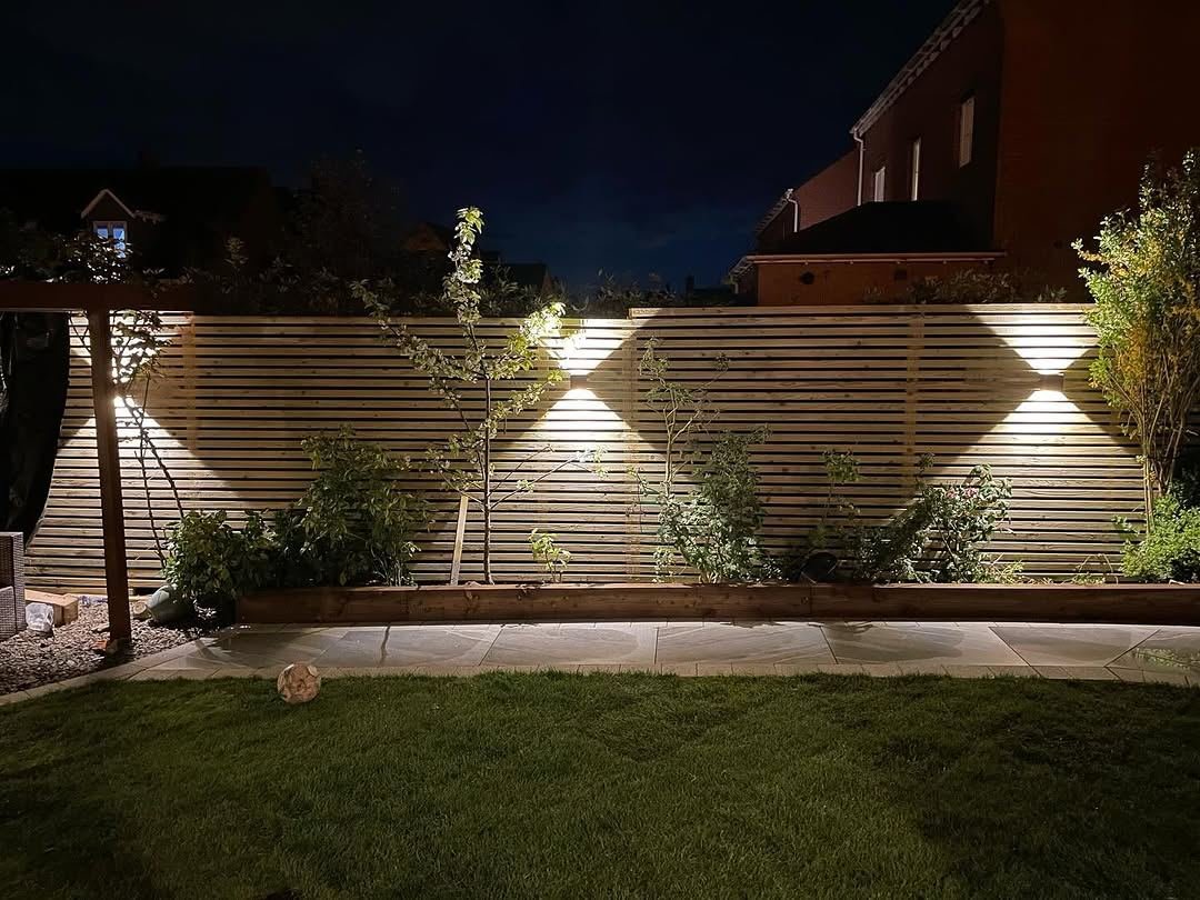 Slatted fence with warm wall lights and young trees at night