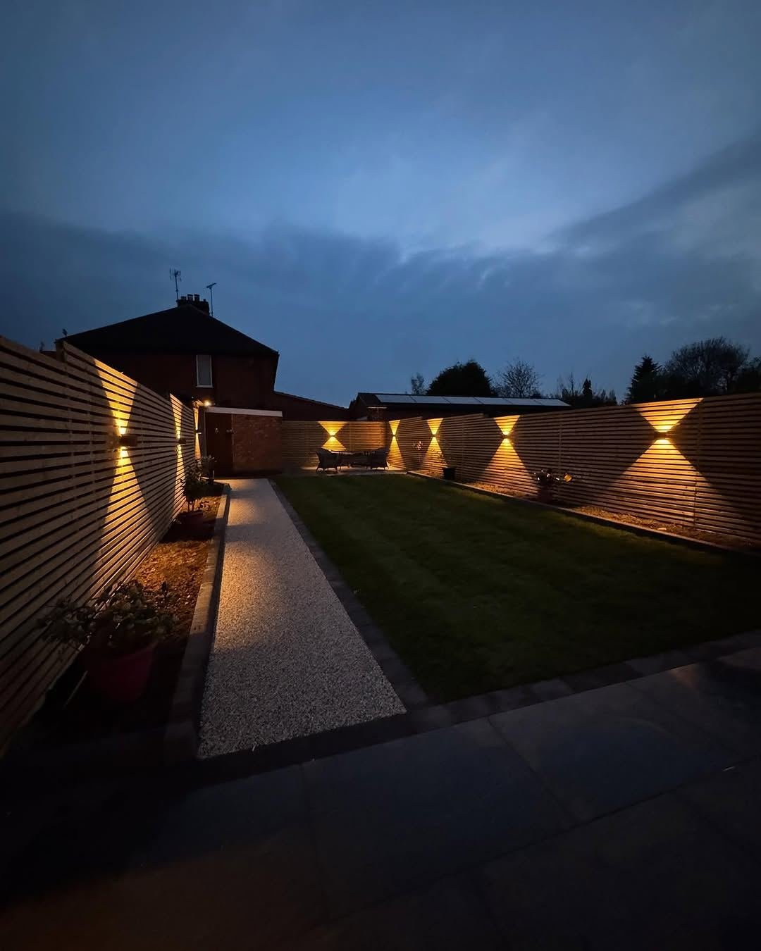 Long garden at night with uplit slatted fencing and a lit resin path